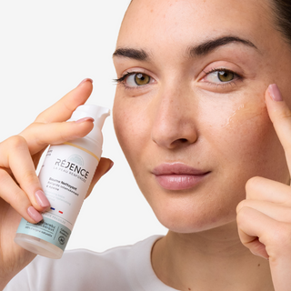 Femme qui s'applique le baume nettoyant Réjence sur la joue en souriant 