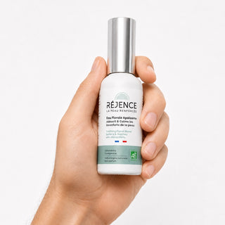 Main tenant le flacon d'Eau Florale Apaisante Réjence, soin hydratant et apaisant à base d'hydrolats bio de calendula, camomille et bleuet pour les peaux sensibles.