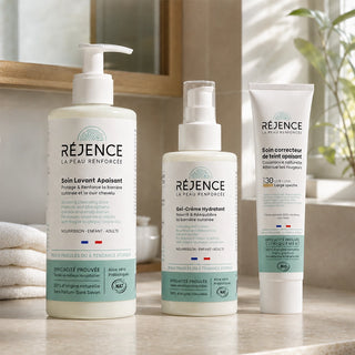 Les trois soins des Essentiels de l'Été Réjence posés dans une salle de bain lumineuse : Soin Lavant Apaisant, Gel-Crème Hydratant et Soin Correcteur de Teint SPF30 pour accompagner la peau sensible tout au long de l'été.