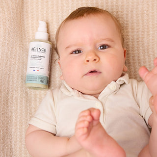 Bébé allongé à côté du Gel-crème hydratant bébé Réjence, soin quotidien pour hydrater et protéger les peaux sensibles dès la naissance.