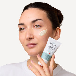 Femme tenant la Cold cream SOS rougeurs et démangeaisons Réjence avec une noisette de crème appliquée sur la joue.