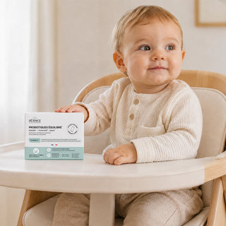 Bébé assis dans une chaise haute à côté d’une boîte de Probiotiques Équilibre Réjence, complément alimentaire en sachets adapté dès la naissance.