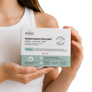 Femme tenant une boîte de Probiotiques Équilibre Réjence, complément alimentaire en 30 sachets associant 3 souches probiotiques et de la vitamine D3 pour soutenir le microbiome intestinal et les défenses naturelles.
