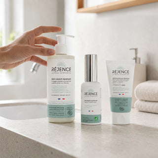 Les trois soins de la routine anti-pelliculaire Réjence posés sur un plan de salle de bain lumineux, avec une main s'apprêtant à utiliser le Soin Lavant Apaisant pour une routine quotidienne des cuirs chevelus sujets aux pellicules.